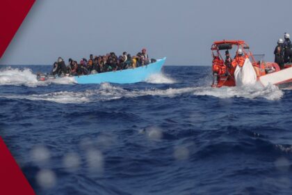 UN human-rights official in blue vest interviews a group of African migrants behind chain-link fence inside a Libyan detention center