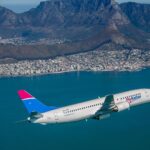 Seamless abstract geometric pattern featuring interlocking hexagonal and triangular shapes in teal and coral hues on a light background