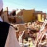 Tall red and white striped lighthouse stands on a rugged rocky coastline, glowing in warm sunset light with calm ocean waters beyond.