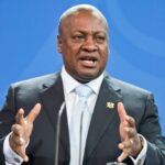 A woman smiling as she lifts a spoonful of colorful smoothie bowl garnished with strawberries, blueberries, raspberries and granola clusters