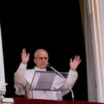 A long sci-fi corridor bathed in purple and blue neon light, its mirror-like floor reflecting the glowing wall panels that line the passage.