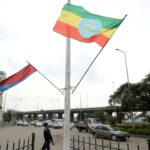 Contemporary abstract artwork featuring overlapping geometric shapes in bold orange, teal and magenta hues against a neutral background