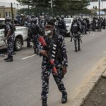 Armed Nigerian riot police in khaki uniforms and helmets confront a crowd of chanting protesters on a smoky Lagos street during political unrest