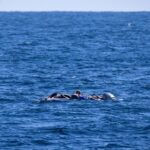 Emergency workers in helmets and high-vis gear carefully lift a dust-covered civilian from a gap in collapsed concrete slabs amid war-damaged buildings.