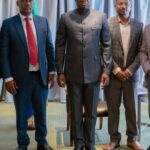 A single shiny red apple resting on a weathered wooden surface, illuminated by natural light.
