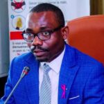 Group of smiling friends gathered around a decorated birthday cake, blowing out the candles together on 18 February 2026
