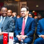 Happy woman in a crisp white blouse posing in front of a textured wooden wall